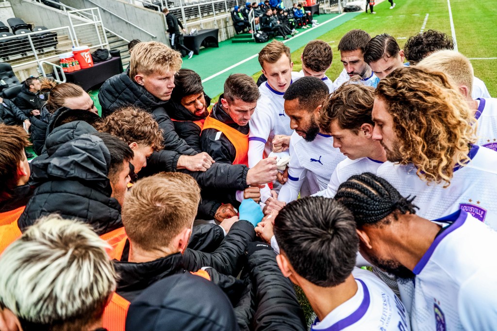A soccer team comes together for a huddle.
